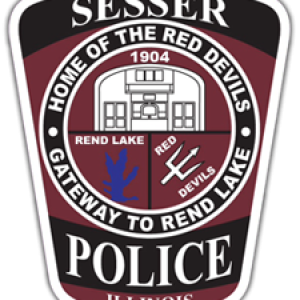 Sesser Police badge. There are three images backed in maroon on it: the city logo, a render of Rend Lake, and a pitchfork with the words Red Devils to represent the sports teams. In white text backed by black it says Sesser Police Illinois and Home of the Red Devils, Gateway to Rend Lake.